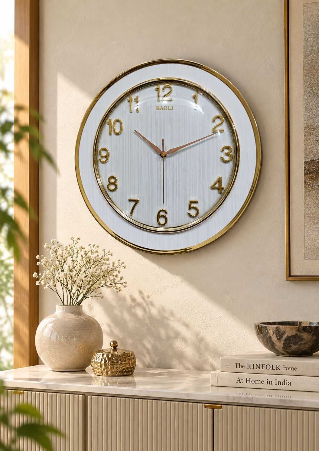 14-inch BAOLI white wood-grain wall clock with gold frame and raised numerals mounted above an elegant dining table in a warm neutral interior.