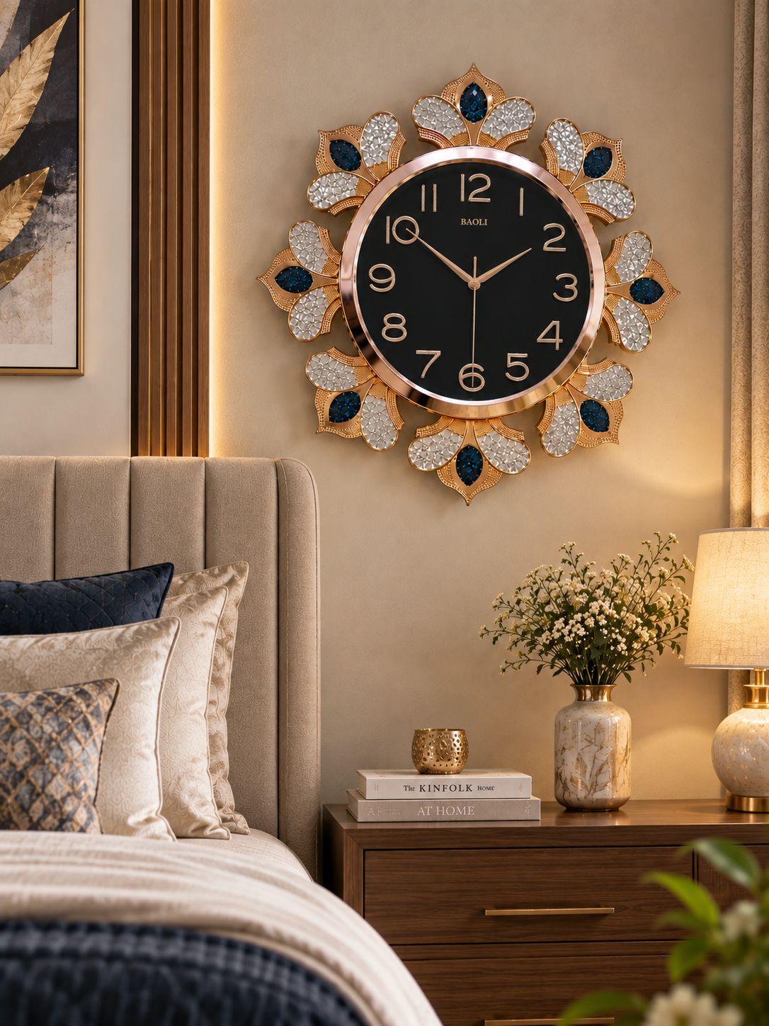 A decorative wall clock with a black face and gold-tone frame, surrounded by leaf-shaped crystal embellishments, mounted above a bed in a styled bedroom setting.