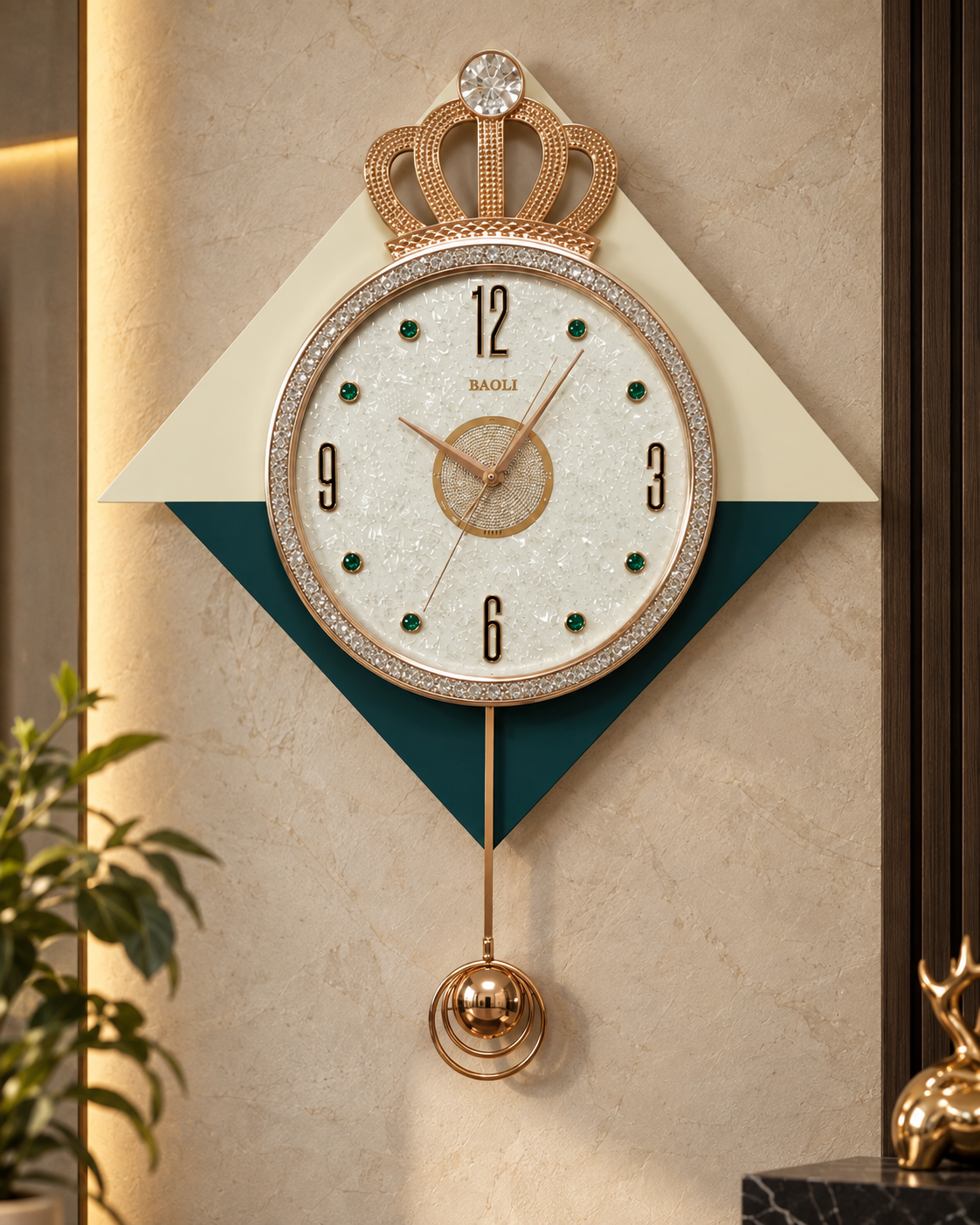 A decorative wall clock with a crown-shaped gold top, a round white face with gold numerals and hands, and a hanging gold bobbin. The clock is mounted on a beige wall with a cream and dark teal geometric backing, with a plant and decor visible at the edges.
