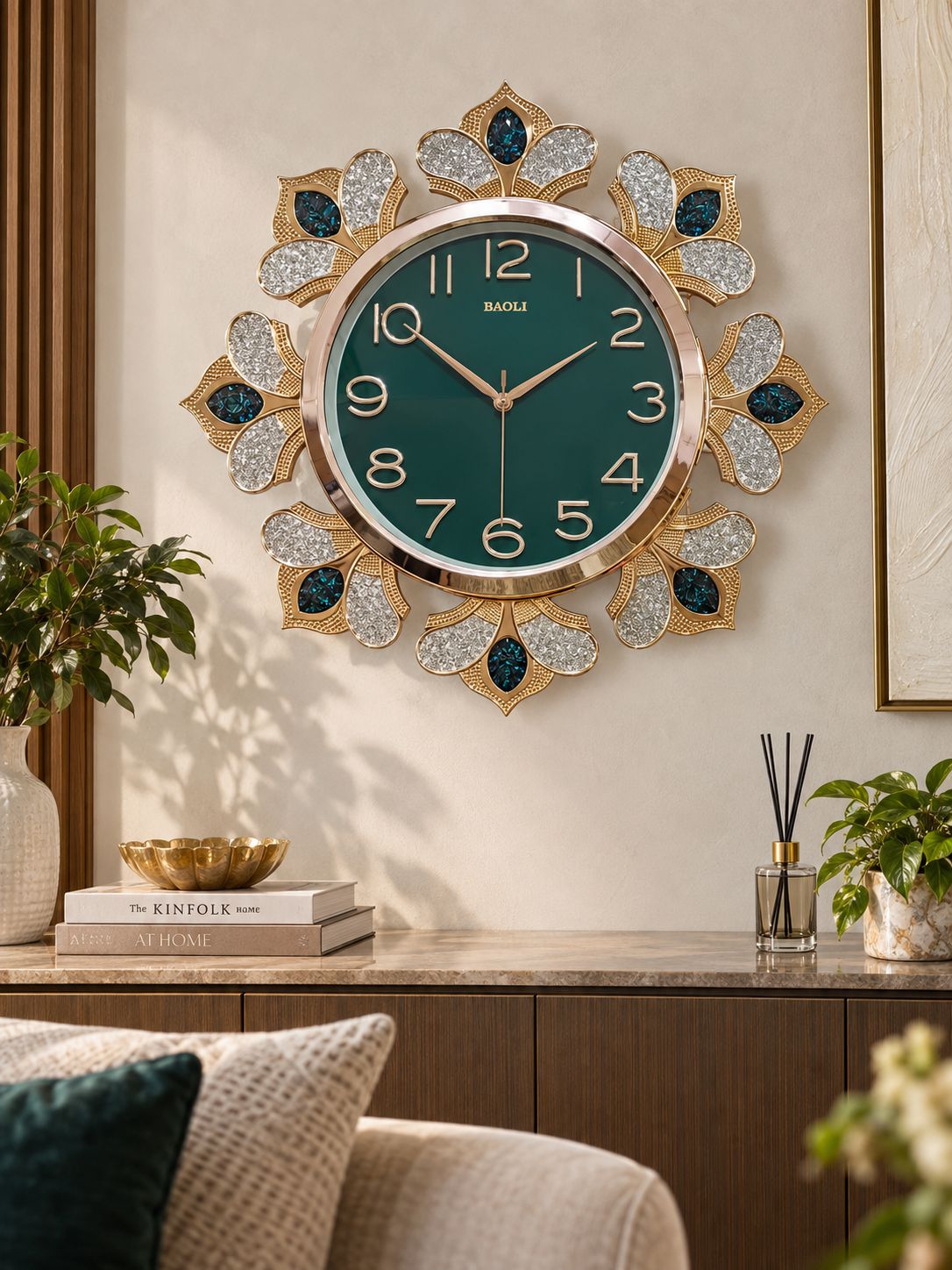 A decorative wall clock with a deep green round face and ornate gold-toned floral frame, mounted on a beige wall above a console table in a styled interior setting.