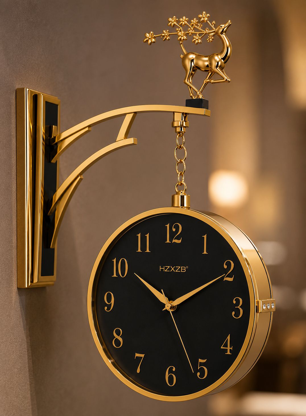 A decorative wall clock with a round black face, gold-tone numerals and hands, mounted on a gold bracket with a hanging deer figurine on a warm blurred interior background.