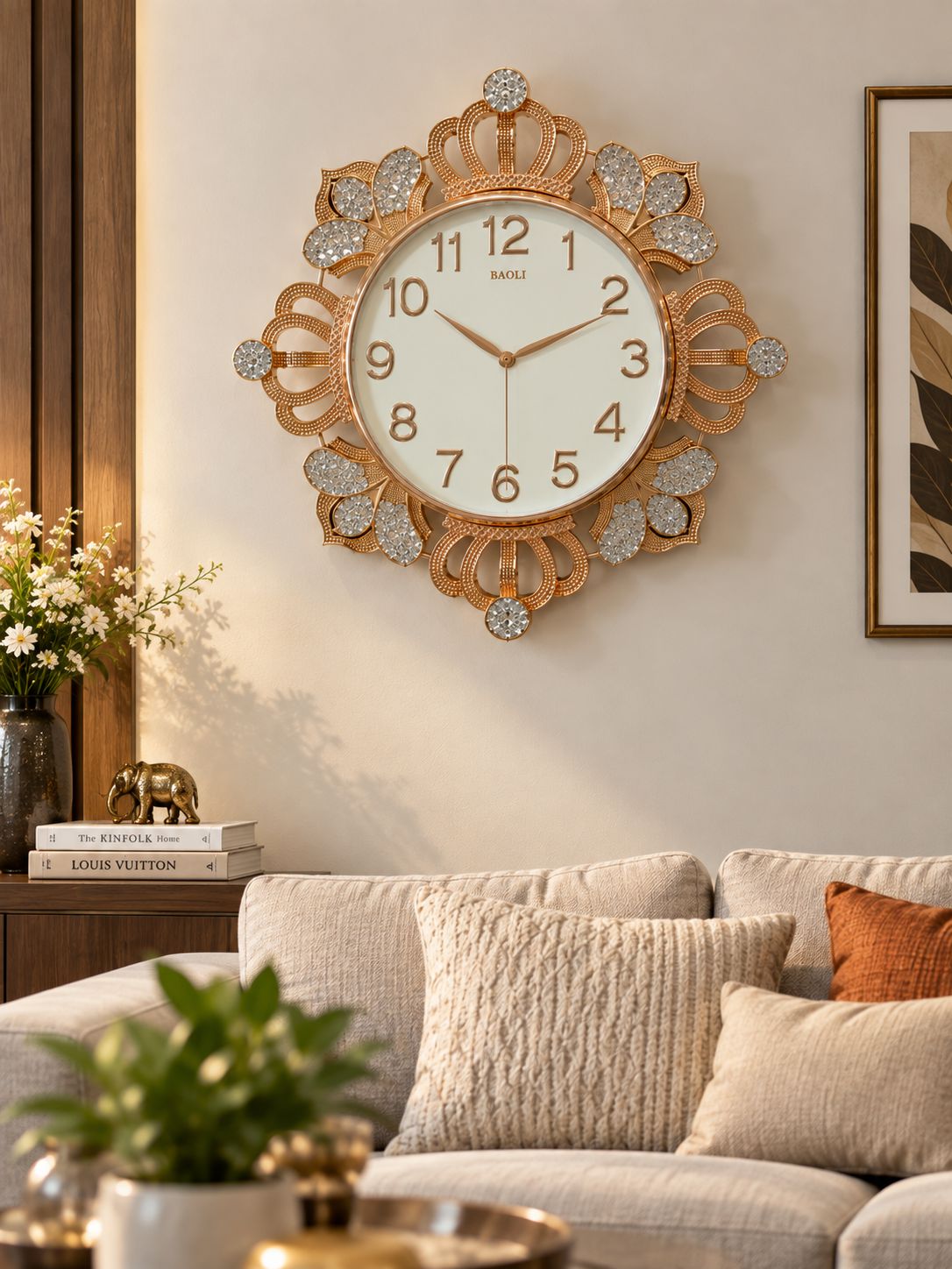 A decorative wall clock with an ornate gold-toned frame and crystal-like embellishments, mounted above a beige sofa in a styled living room.