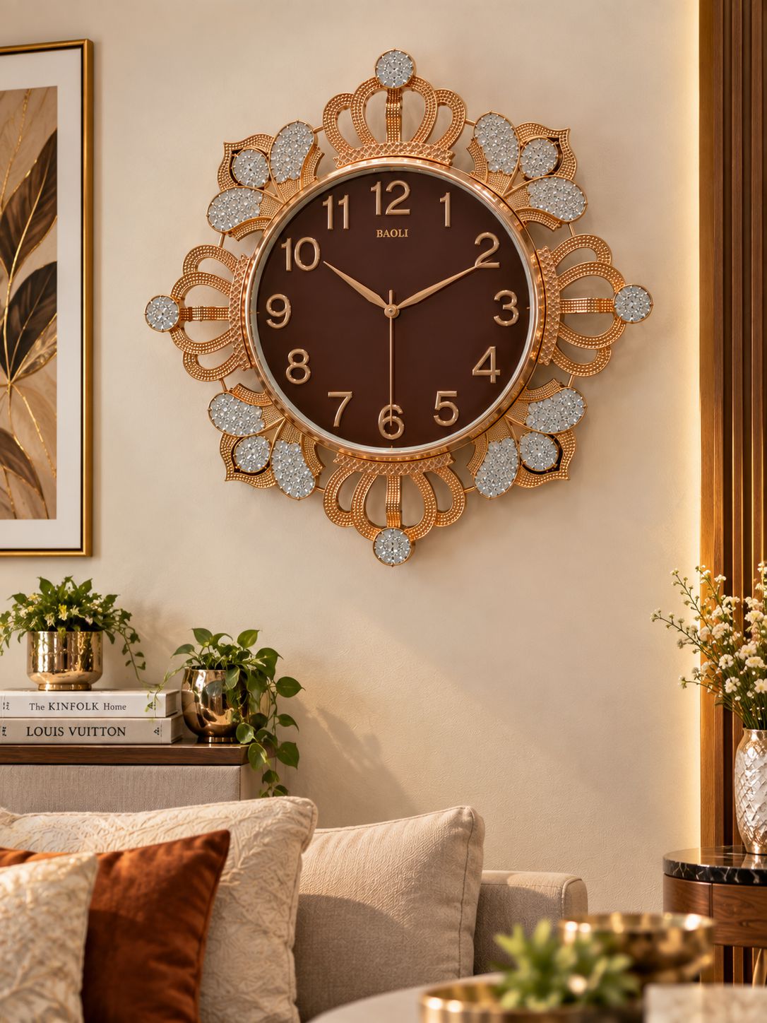 A large decorative wall clock with an ornate gold-tone frame and crystal-like accents, mounted on a beige wall in a styled living room above a sofa.