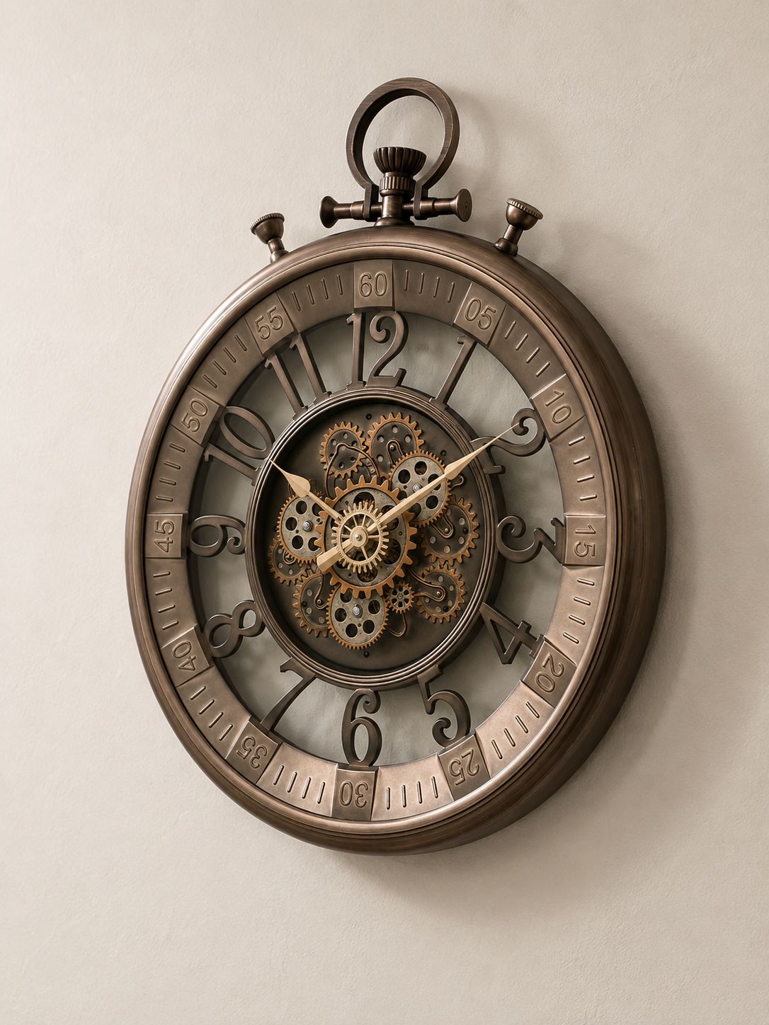 A large round wall clock styled like a vintage pocket watch, featuring a bronze-toned metal frame, exposed internal gears, and ornate Arabic numerals, mounted on a plain beige wall.