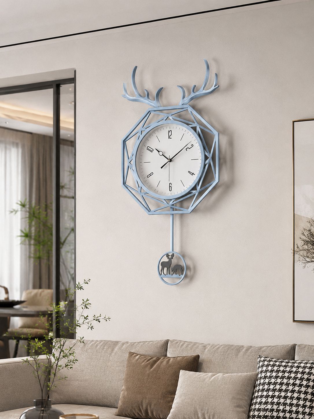 A light blue geometric wall clock with a deer head silhouette and hanging bell, mounted on a beige wall above a sofa in a modern living room.