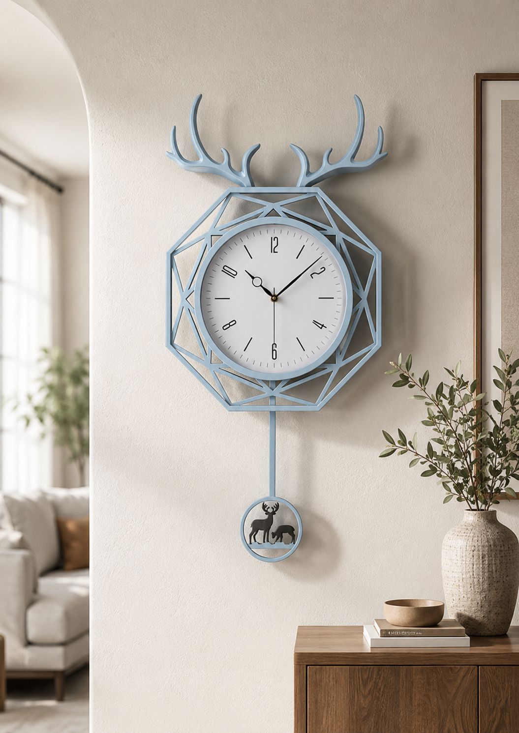 A light blue geometric wall clock with antler details on the top and a hanging deer figure below, mounted on a beige wall in a styled interior setting.