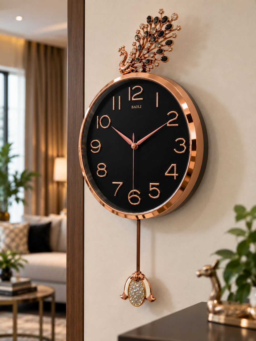 A luxury wall clock with a rose gold frame, black dial, and a decorative peacock topper, shown hanging on a beige wall in a modern living room setting.