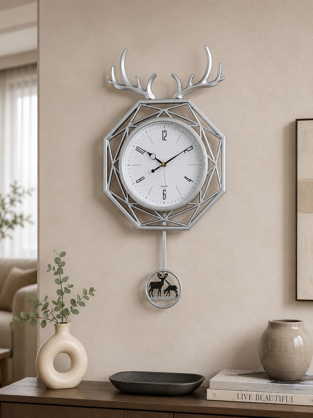 A modern geometric wall clock with a deer head frame, mounted on a beige wall above a console table with decorative vases and books.