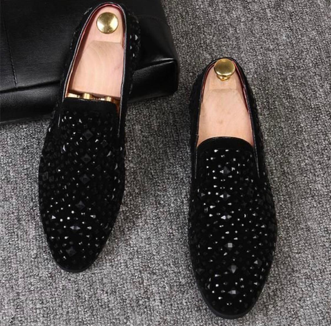 A pair of black studded moccasin loafers for men, featuring a suede upper and a rubber outsole, displayed against a grey background.