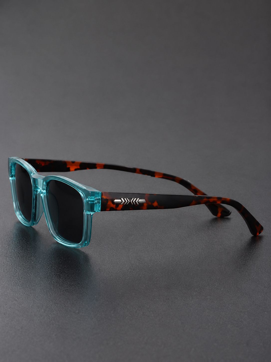 A pair of square sunglasses with translucent aqua blue front frames and dark tortoiseshell temples, resting on a dark gray surface.