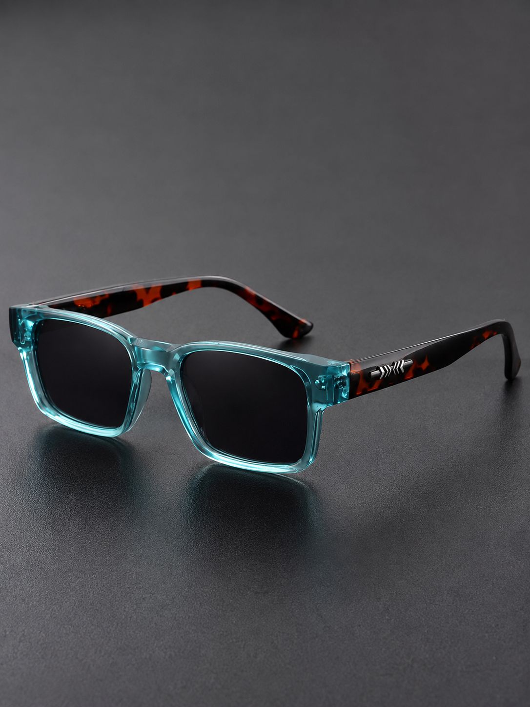 A pair of sunglasses with translucent aqua blue front frames, dark lenses, and black temples featuring a red-orange tortoiseshell pattern, displayed on a dark gray surface.