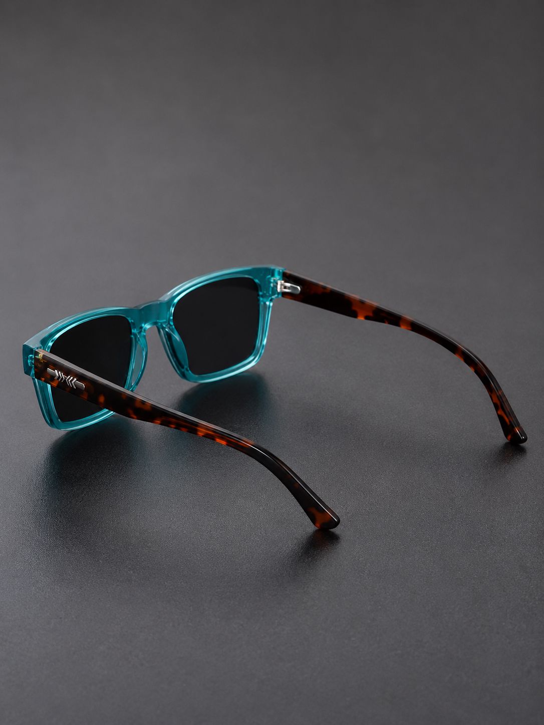 A pair of sunglasses with translucent teal-blue front frames and dark tortoiseshell temples, displayed on a dark gray surface.