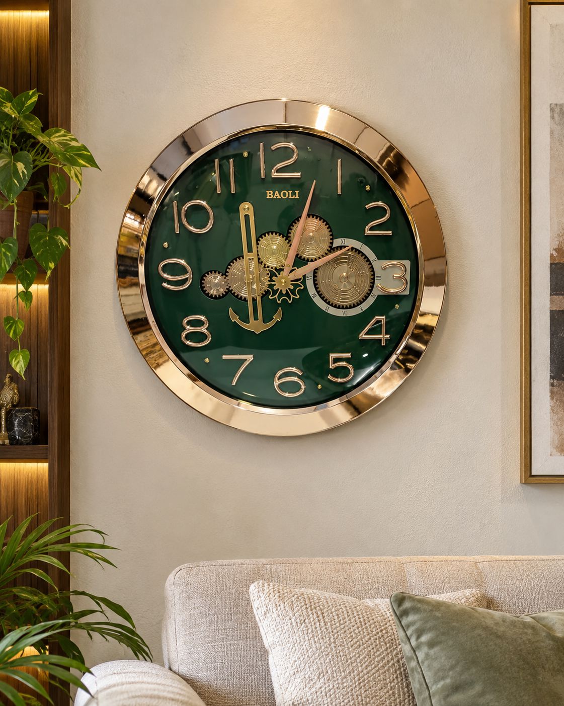 A round BAOLI wall clock with a dark green dial and gold-tone frame, mounted on a beige wall above a sofa with pillows, with a plant and framed art nearby.