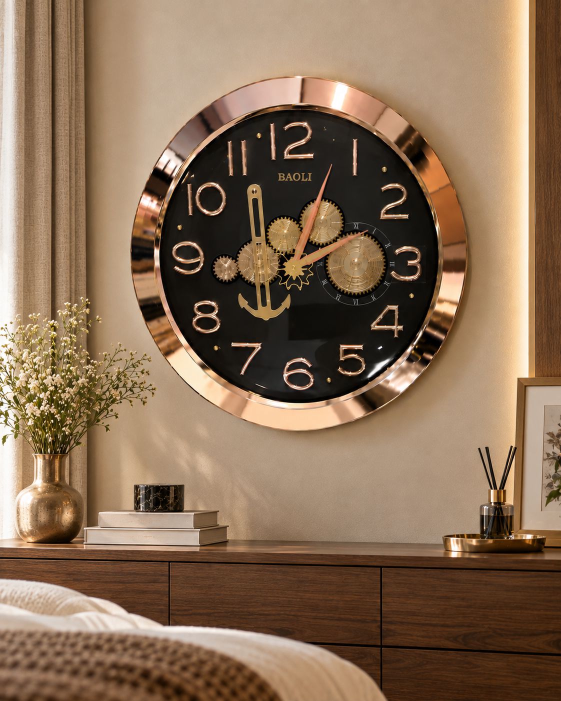 A round wall clock with a black face, gold-tone gears and hands, and a shiny rose-gold metallic frame, mounted on a beige wall above a wooden console table in a styled bedroom setting.