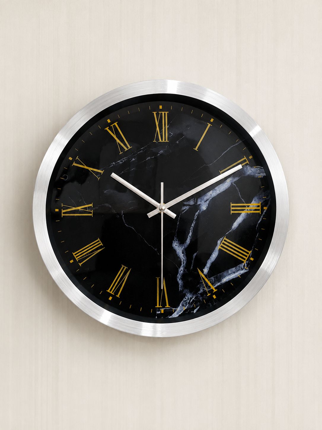 A round wall clock with a black marble-patterned face, gold Roman numerals, silver-tone hands, and a brushed silver metal frame, mounted on a light beige textured wall.