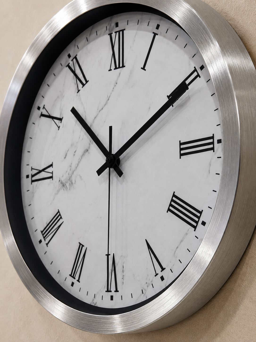 A round wall clock with a brushed silver metal frame, a white marble-patterned dial, and black Roman numerals and hands.