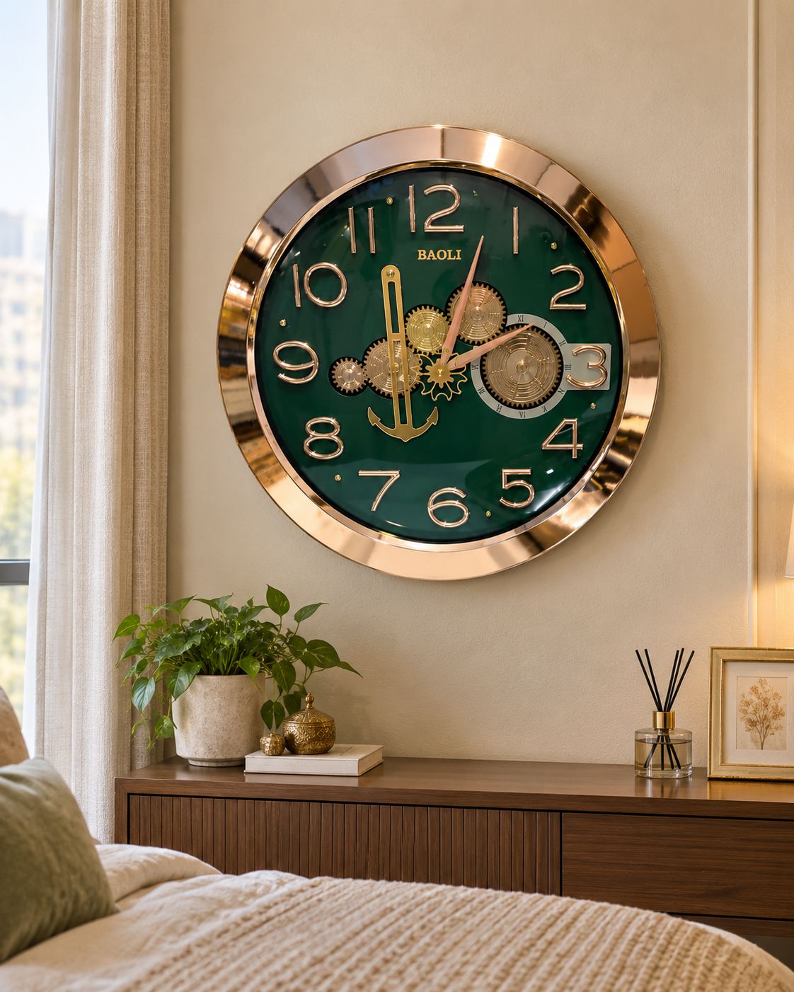 A round wall clock with a dark green face, gold-tone bezel, and gold mechanical gear design in the center, mounted on a beige wall above a wooden nightstand in a styled bedroom.