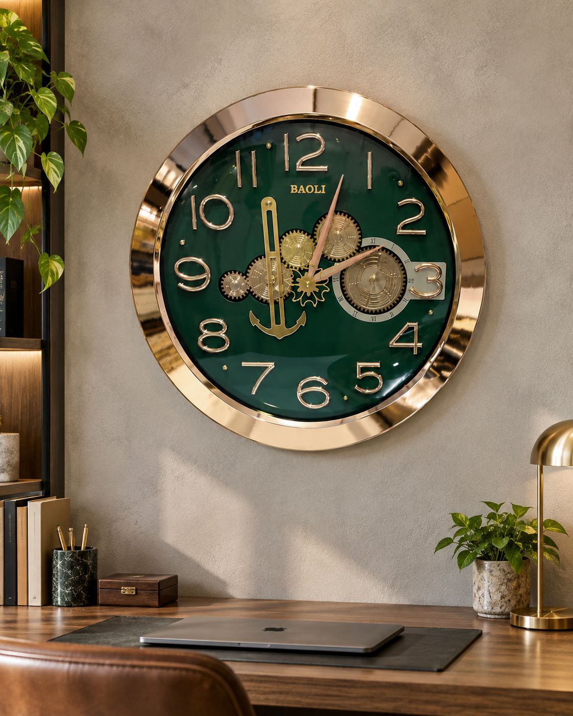A round wall clock with a polished gold-tone frame and a dark green face, mounted on a textured gray wall above a wooden desk. The clock features gold Arabic numerals, decorative gold gears and anchor details on the dial, and the BAGLI brand name printed above the 12.