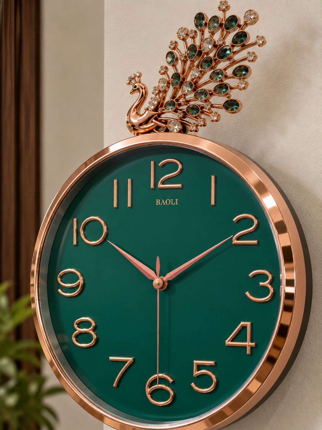 A round wall clock with a rose gold frame and a dark green dial, featuring a decorative peacock topper embellished with green gemstones. The brand name 'BAOLI' is printed on the dial.