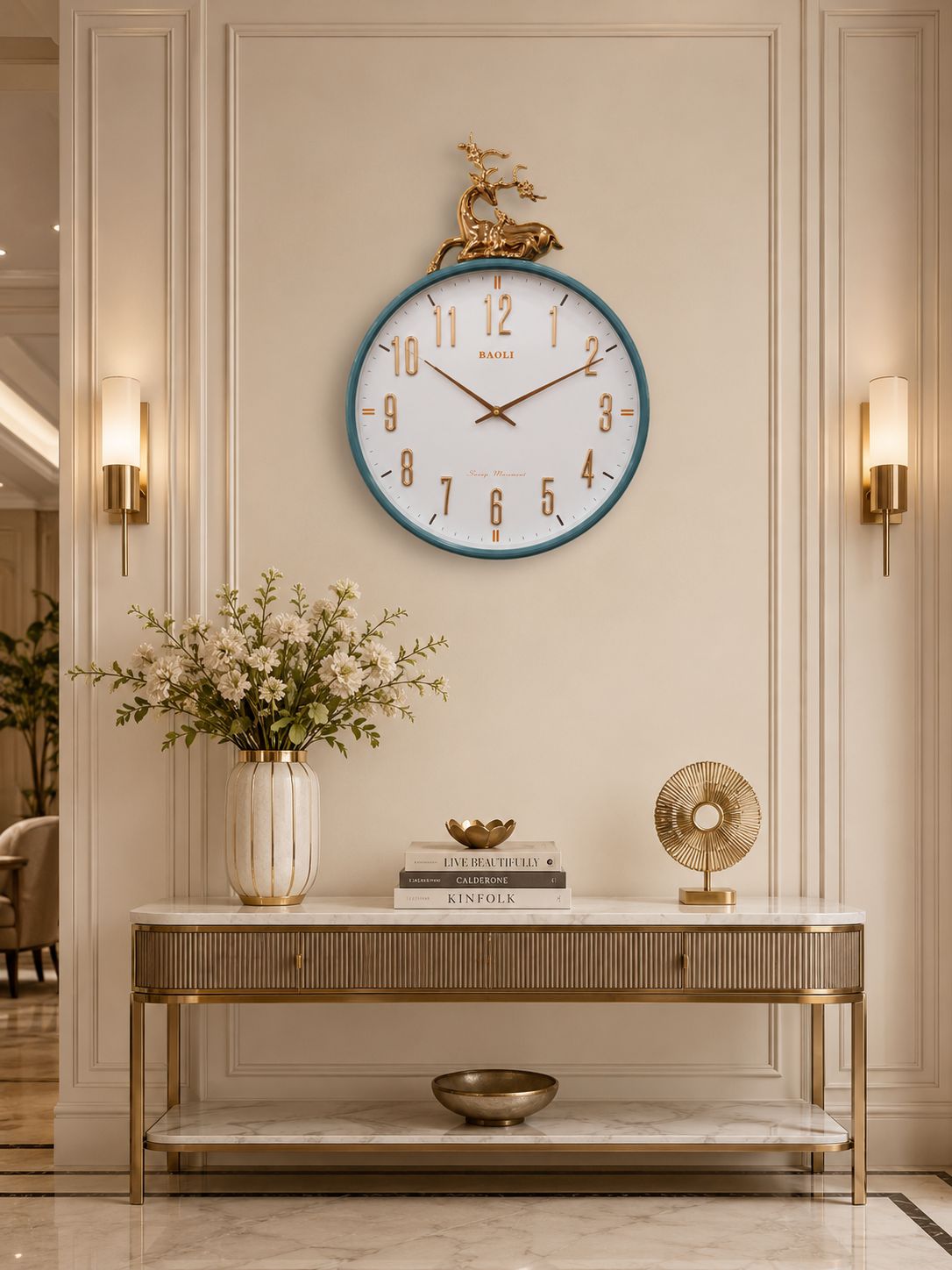 A round wall clock with a white face, blue rim, and gold details hangs above a console table in a beige interior setting.