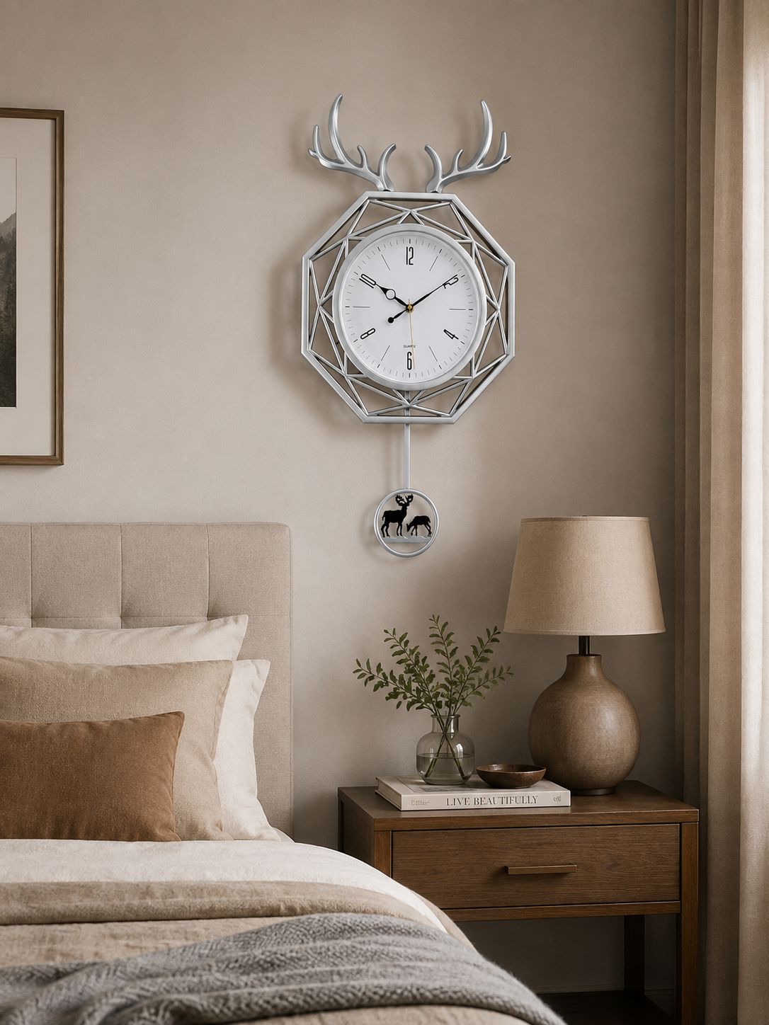 A silver geometric wall clock with deer antler motifs and a hanging deer emblem, displayed above a bed in a styled bedroom setting.
