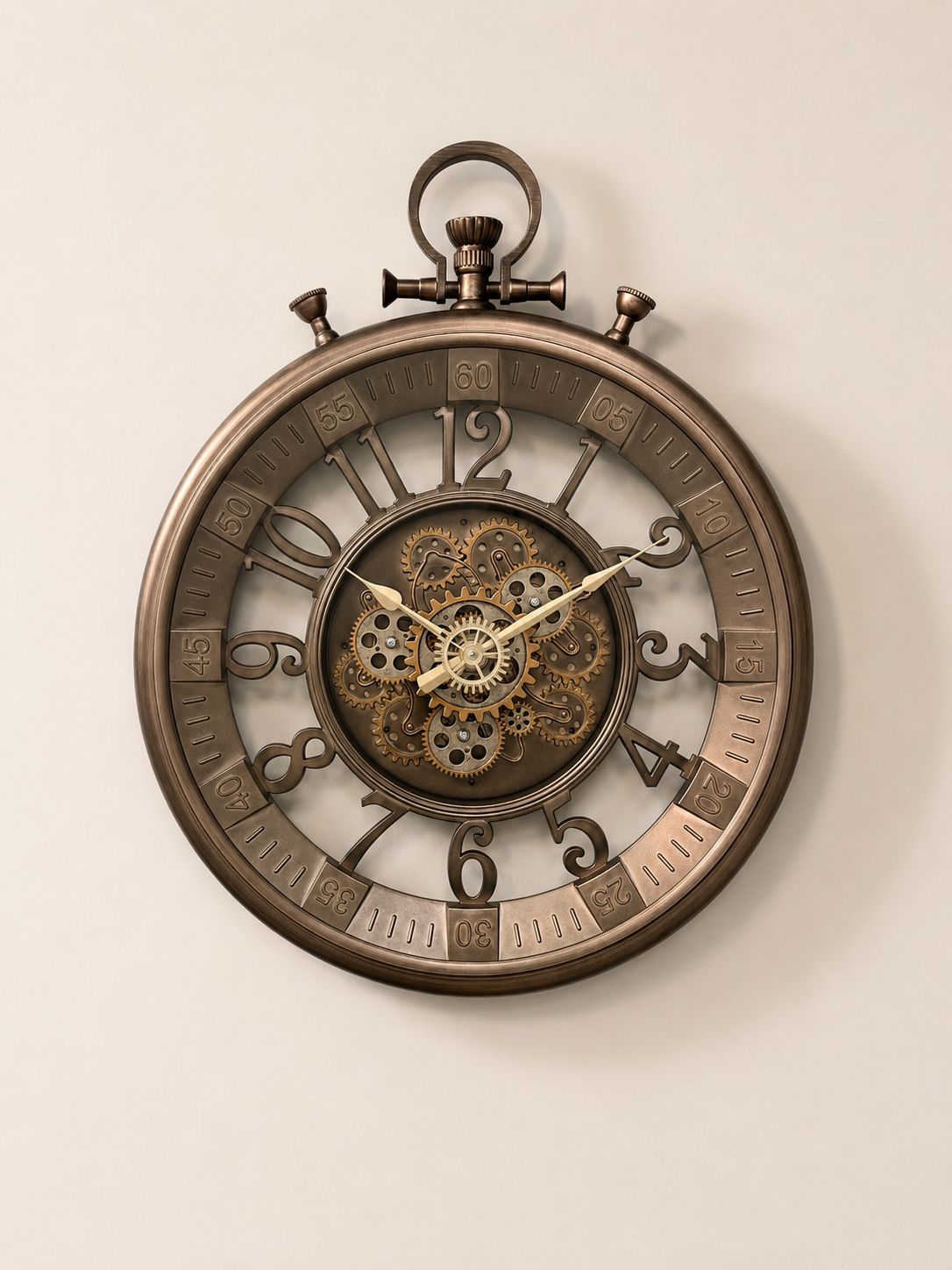 A steampunk-style wall clock with a large round bronze-toned frame, exposed internal gears and cogs at the center, decorative Roman numerals, and ornate hands, shown hanging against a plain light beige wall.
