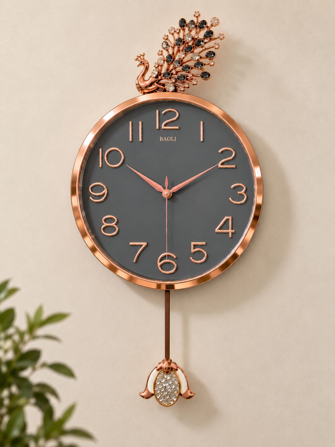 A wall clock with a rose gold peacock top and bottom ornament, featuring a dark gray face and matching rose gold numerals and hands, mounted on a beige wall.