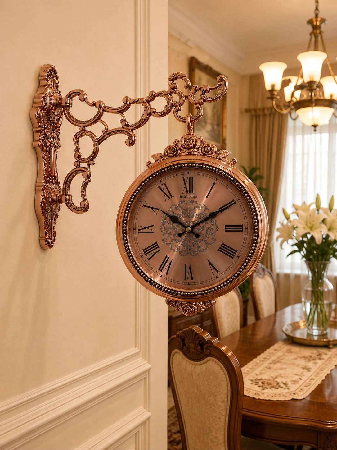 An ornate bronze wall clock with a decorative scrollwork bracket and a round face, mounted on a cream-colored wall in a dining room setting.