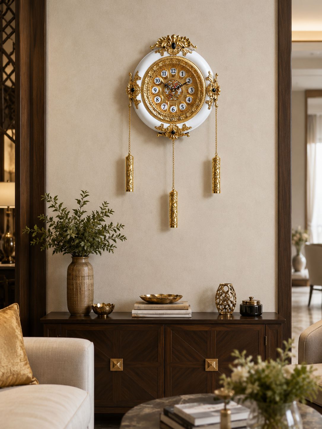 An ornate round wall clock with a white face, gold frame, and hanging gold tassels, mounted on a beige wall above a dark wood console in a styled living room.