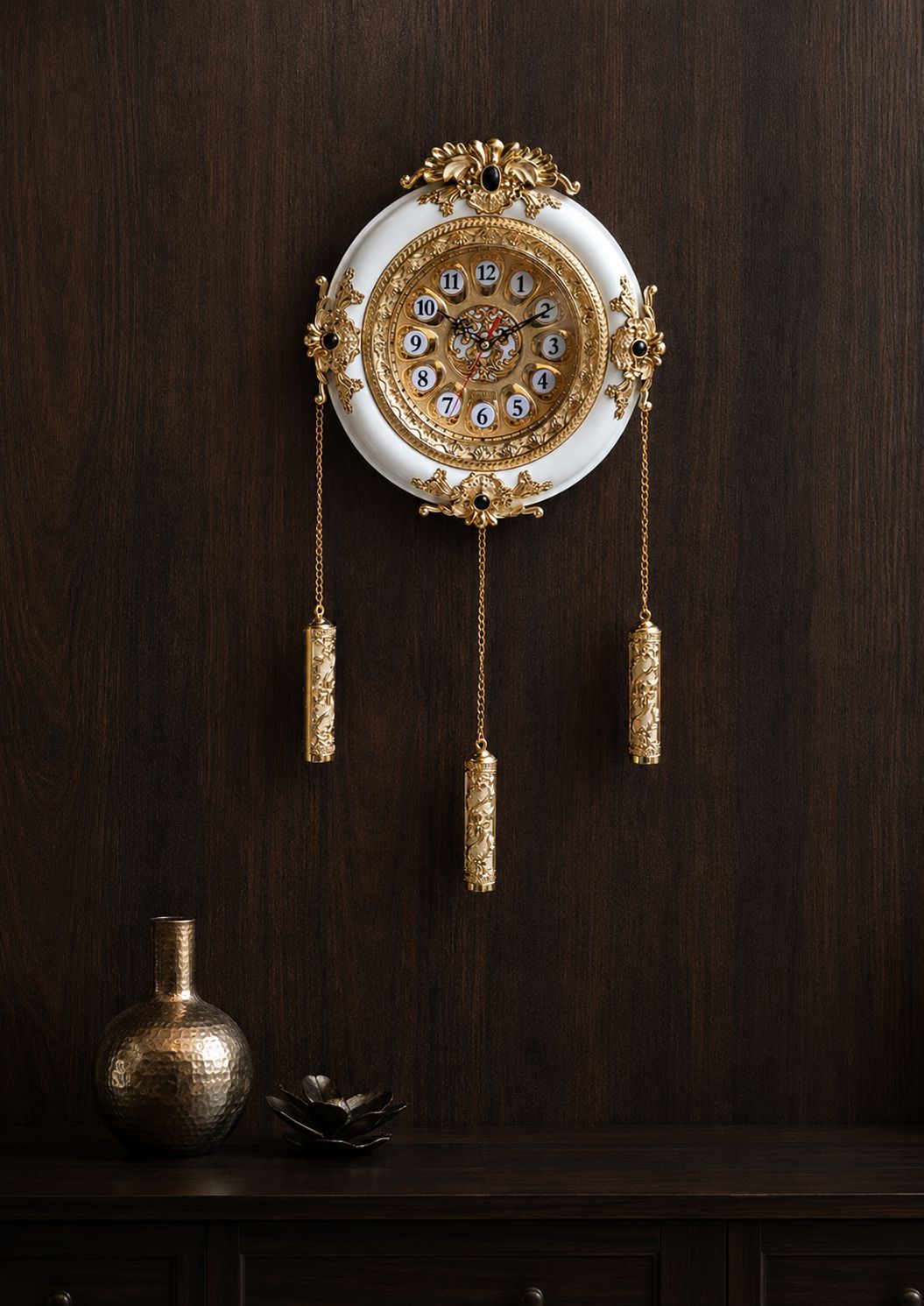 An ornate wall clock with a white circular face and extensive gold filigree detailing, hanging on a dark wood-paneled wall above a dark wooden console table with decorative vases.
