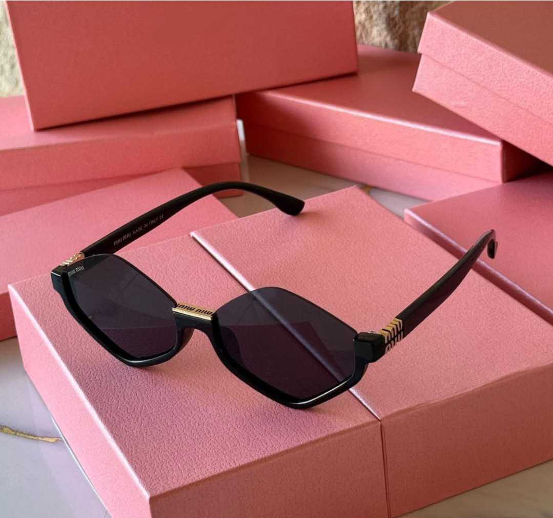 Black diamond-shaped geometric sunglasses with gold accents on a pink background.