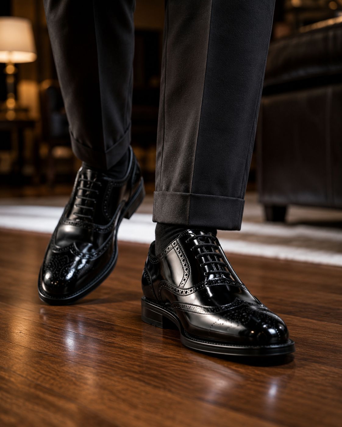Black dress shoes worn with dark pants on a wooden floor.