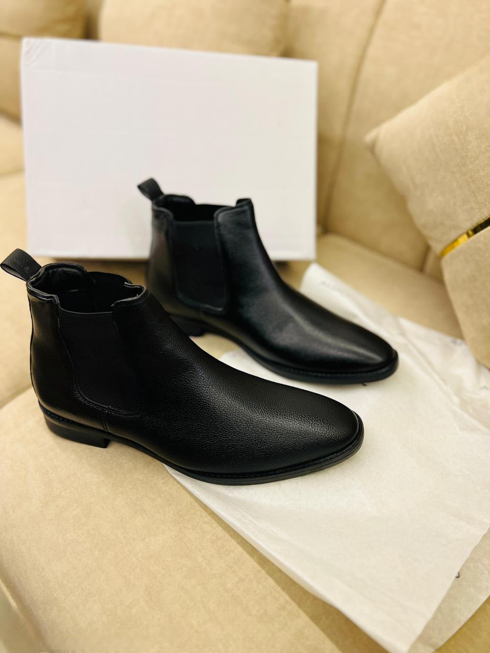 Black leather boots on a beige sofa with a white box in the background