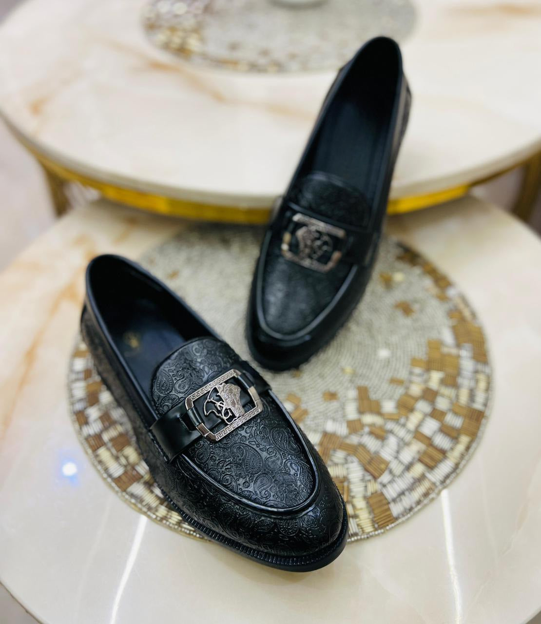 Black loafers with decorative buckles on a marble surface
