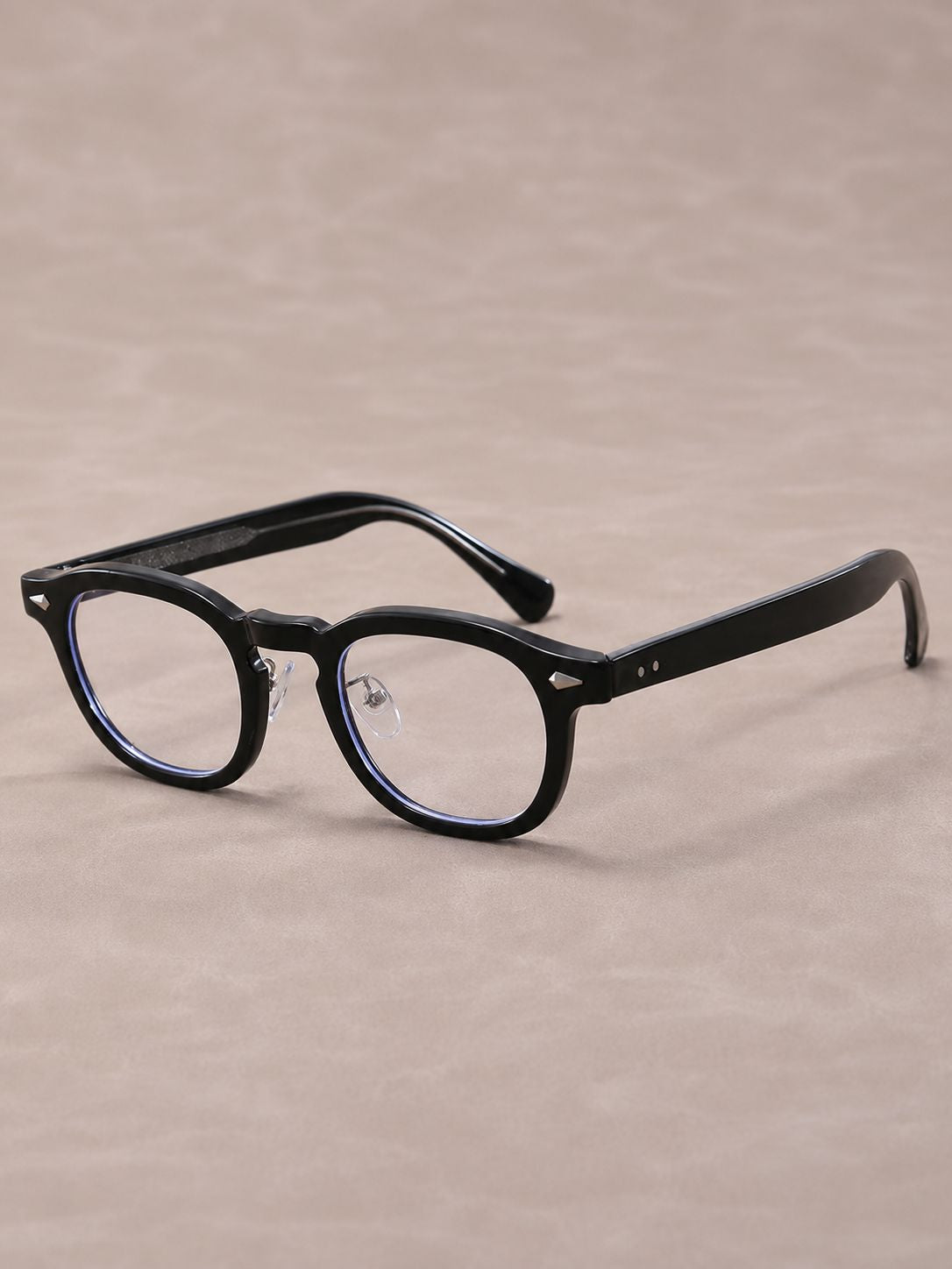 Black round-frame eyeglasses with clear lenses and subtle blue inner rim accents, photographed on a warm beige textured background.