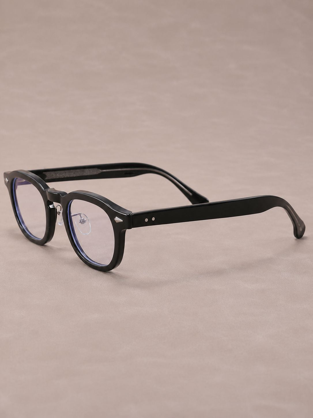 Black round-frame eyeglasses with clear lenses and thin metal hinges, displayed on a neutral beige background.