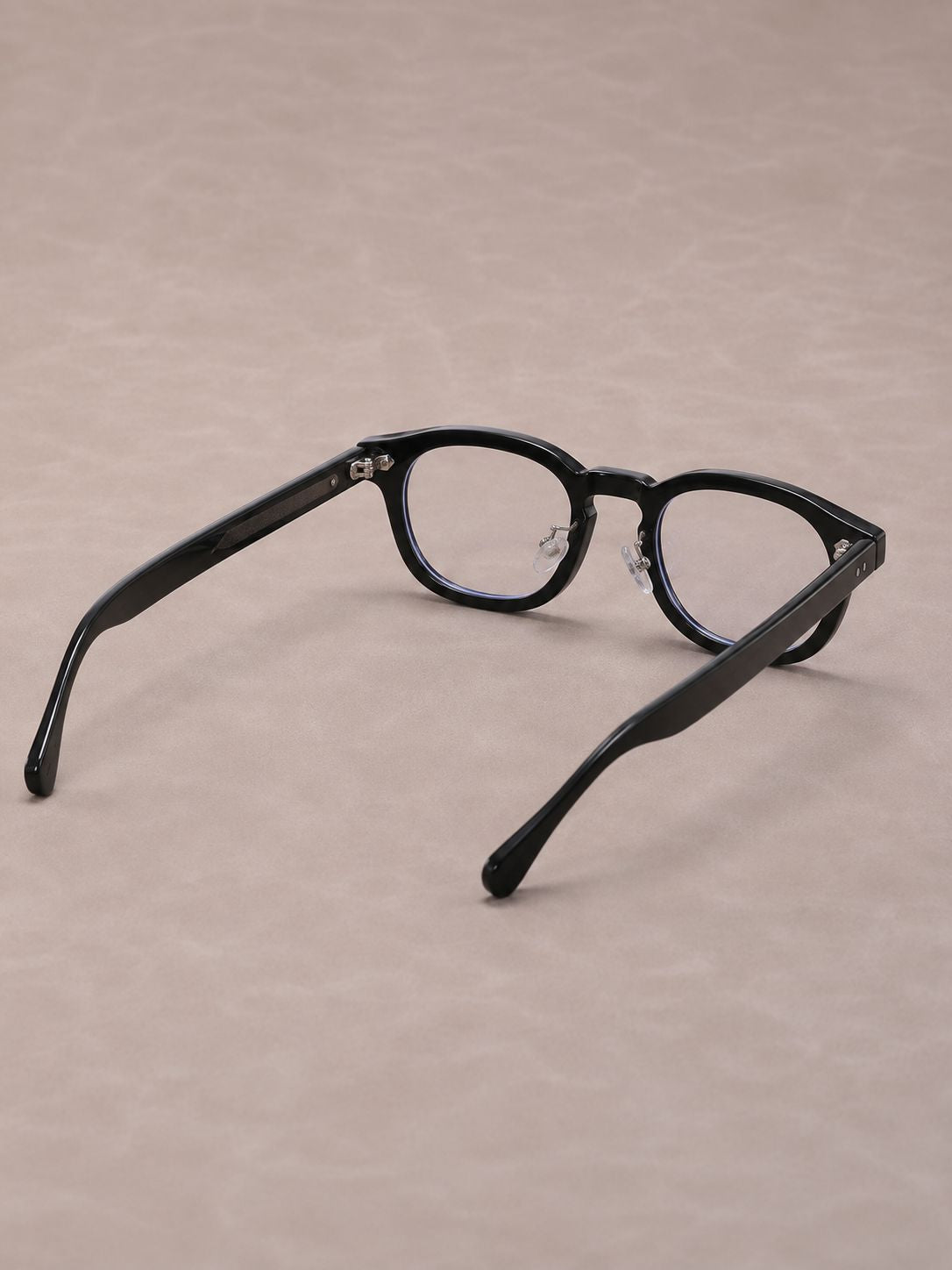 Black round-frame eyeglasses with clear lenses, displayed on a textured beige background.
