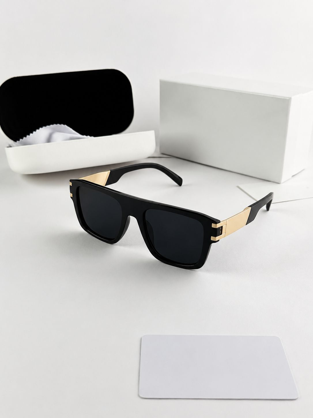 Black sunglasses with gold accents on a white surface with a case and box in the background.