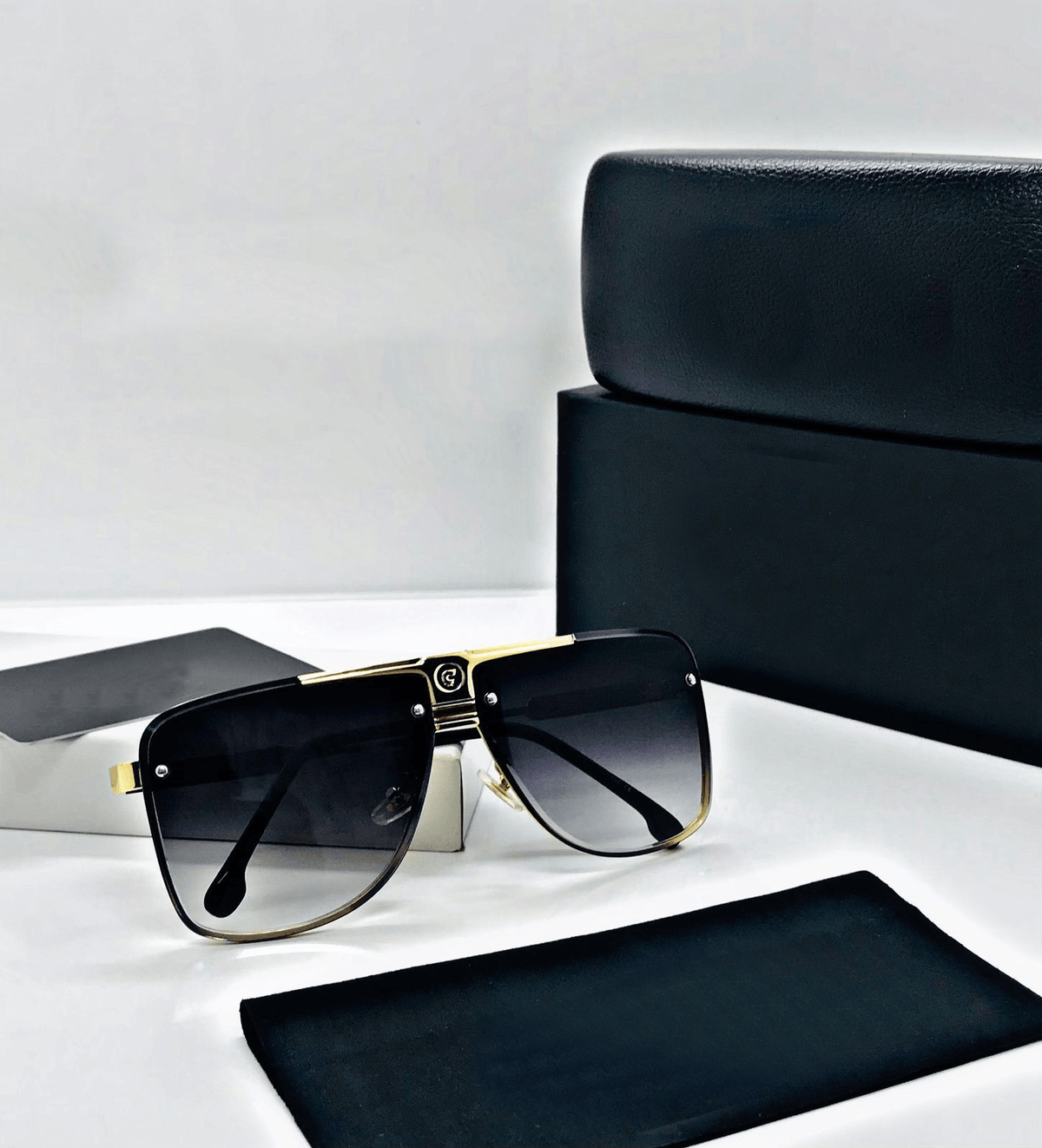 Black sunglasses with gold frame on a white surface with black case and box.
