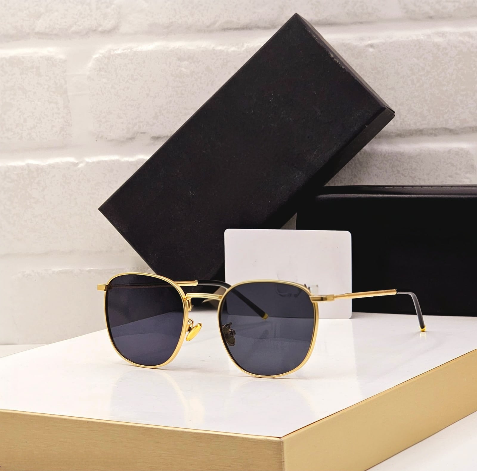 Bold black oversized round sunglasses with dark lenses and a prominent gold metal bar detail.
