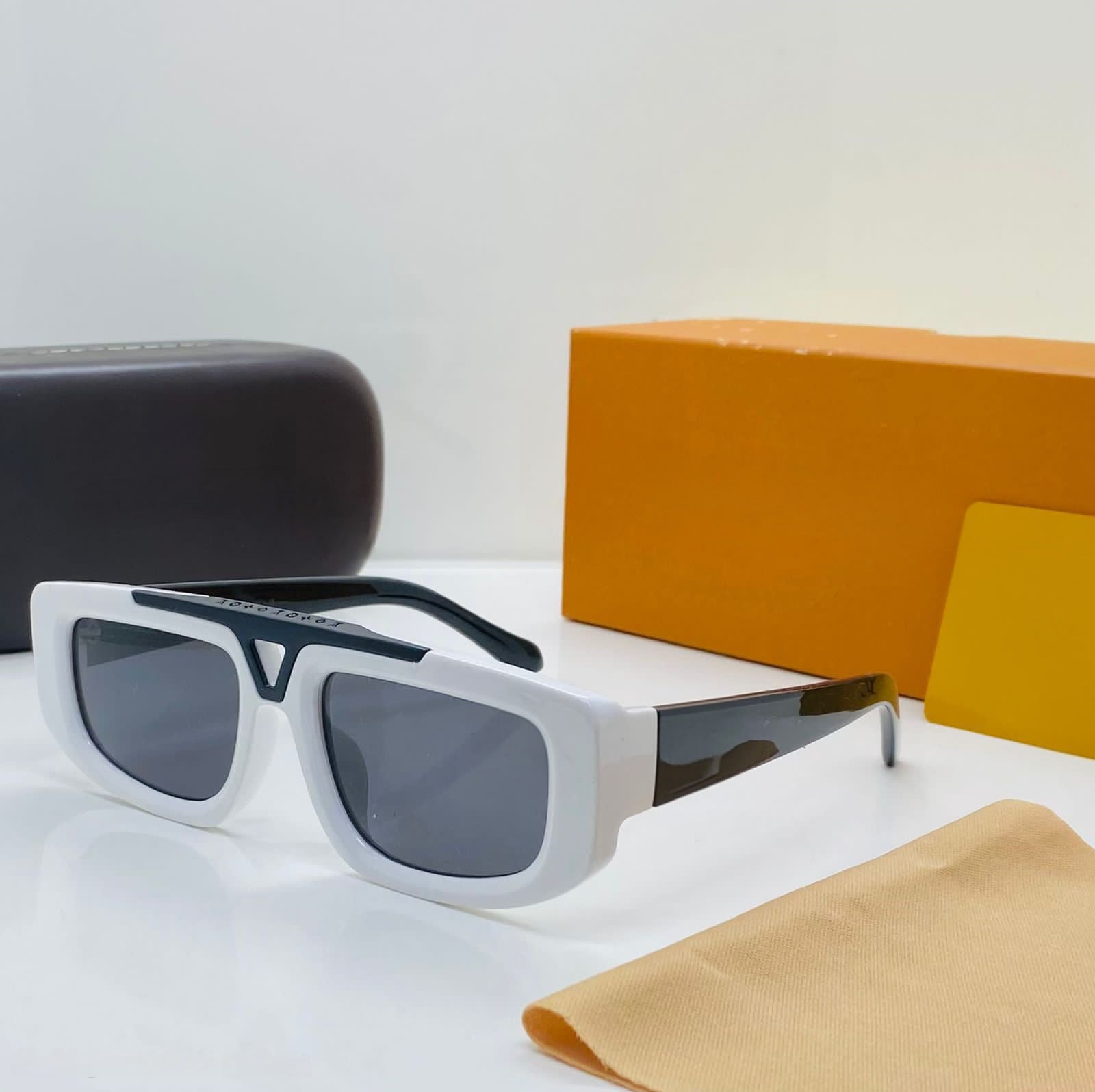 Bold white chunky square sunglasses with black contrast top bar and temples, displayed with luxury yellow and brown packaging.