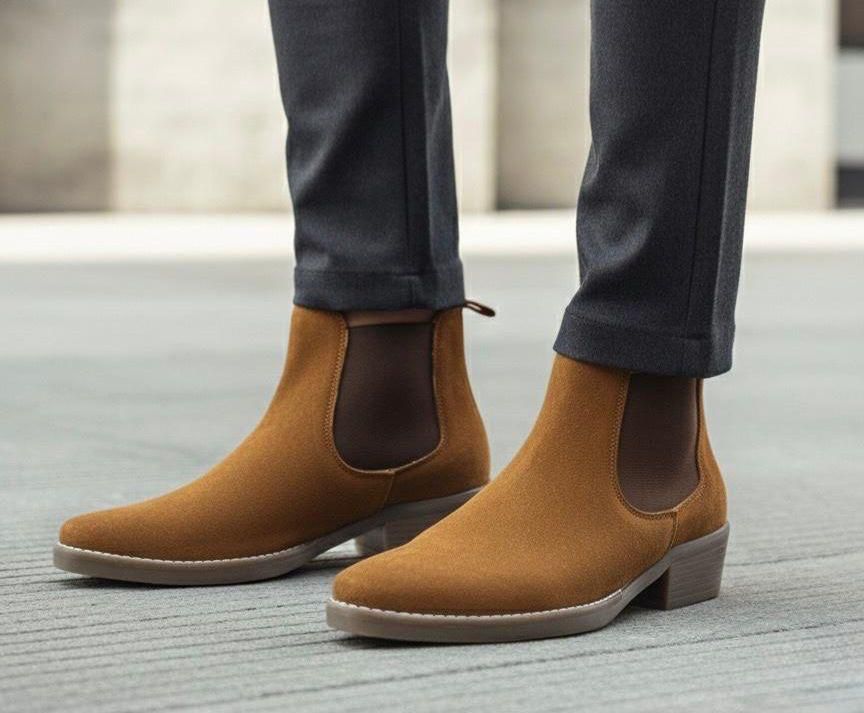 Brown suede Chelsea boots worn with dark pants on a neutral background