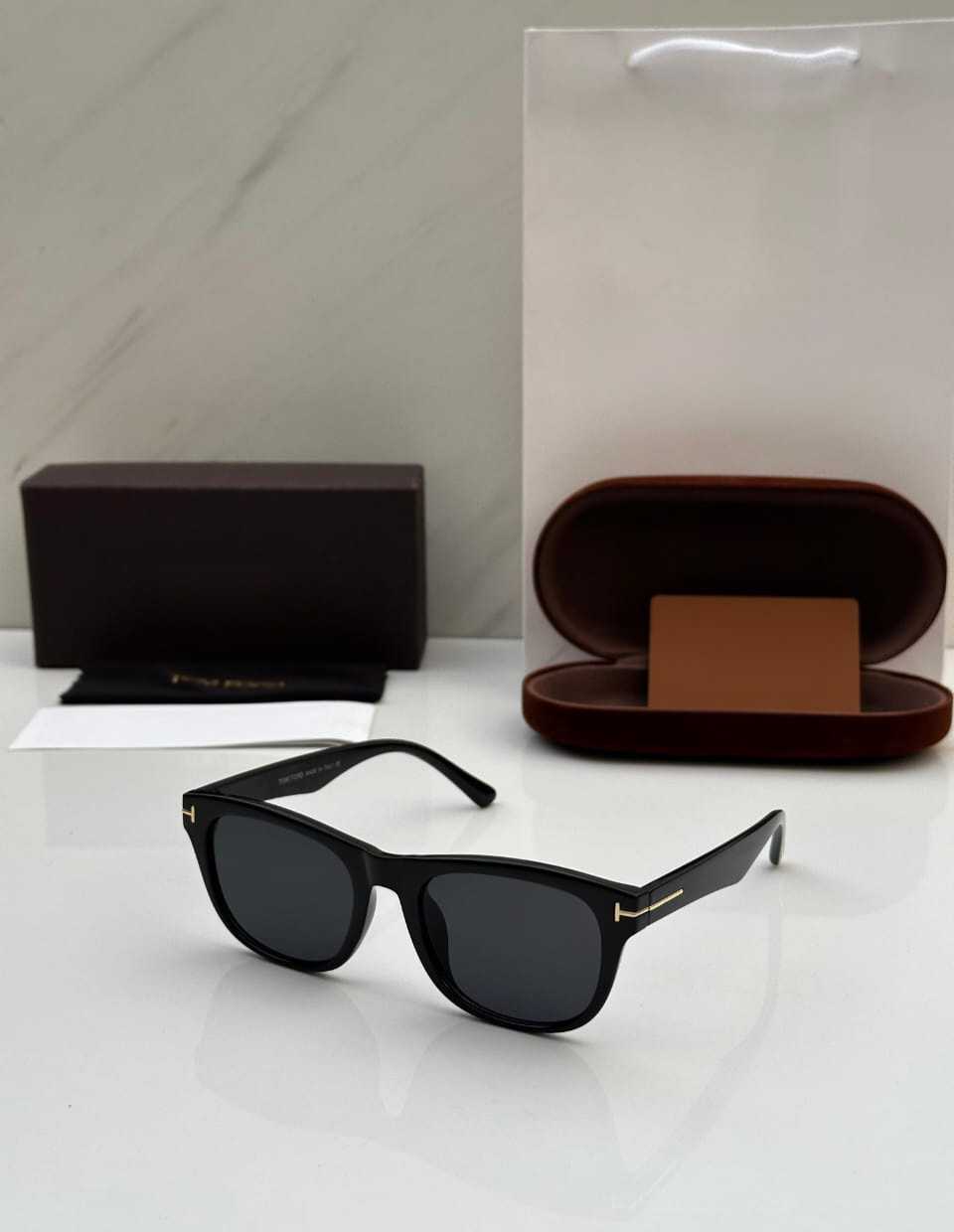 Classic black square sunglasses with dark lenses and gold 'T' accents on the temples.