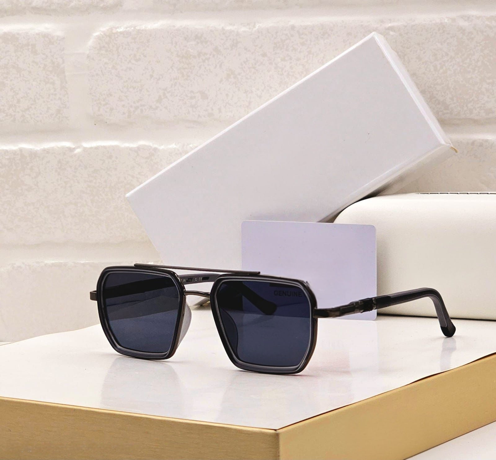 Classic black square sunglasses with dark lenses displayed on a gold surface.