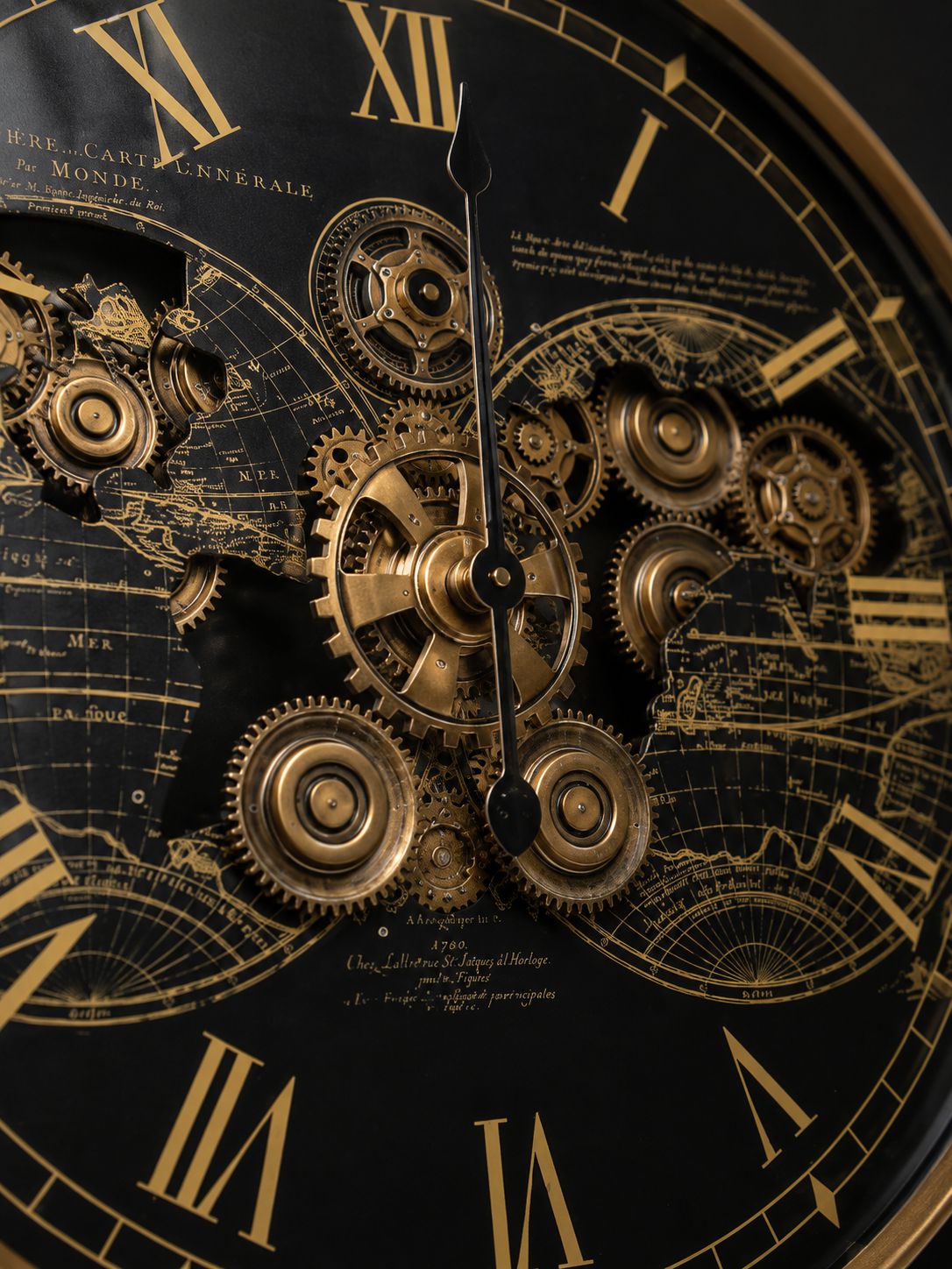 Close-up of a decorative wall clock face with Roman numerals, intricate gold gears, map illustrations, and black hands on a dark background.