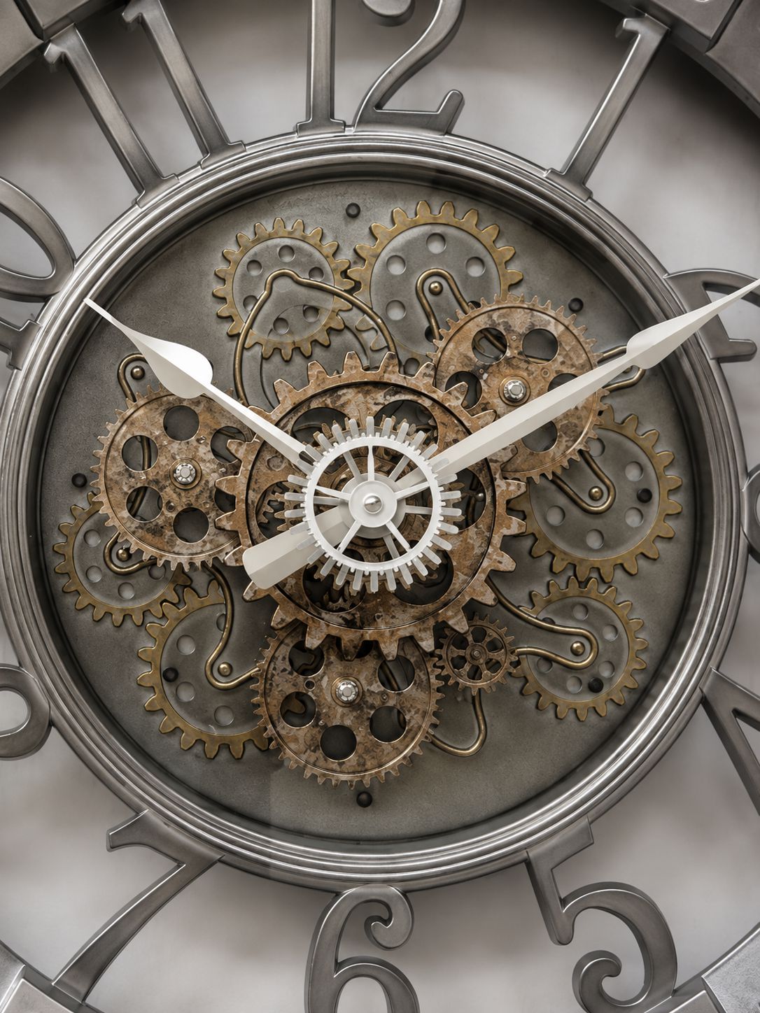 Close-up of a decorative wall clock face with exposed mechanical gears and cogs, silver-tone numerals, and white hands.