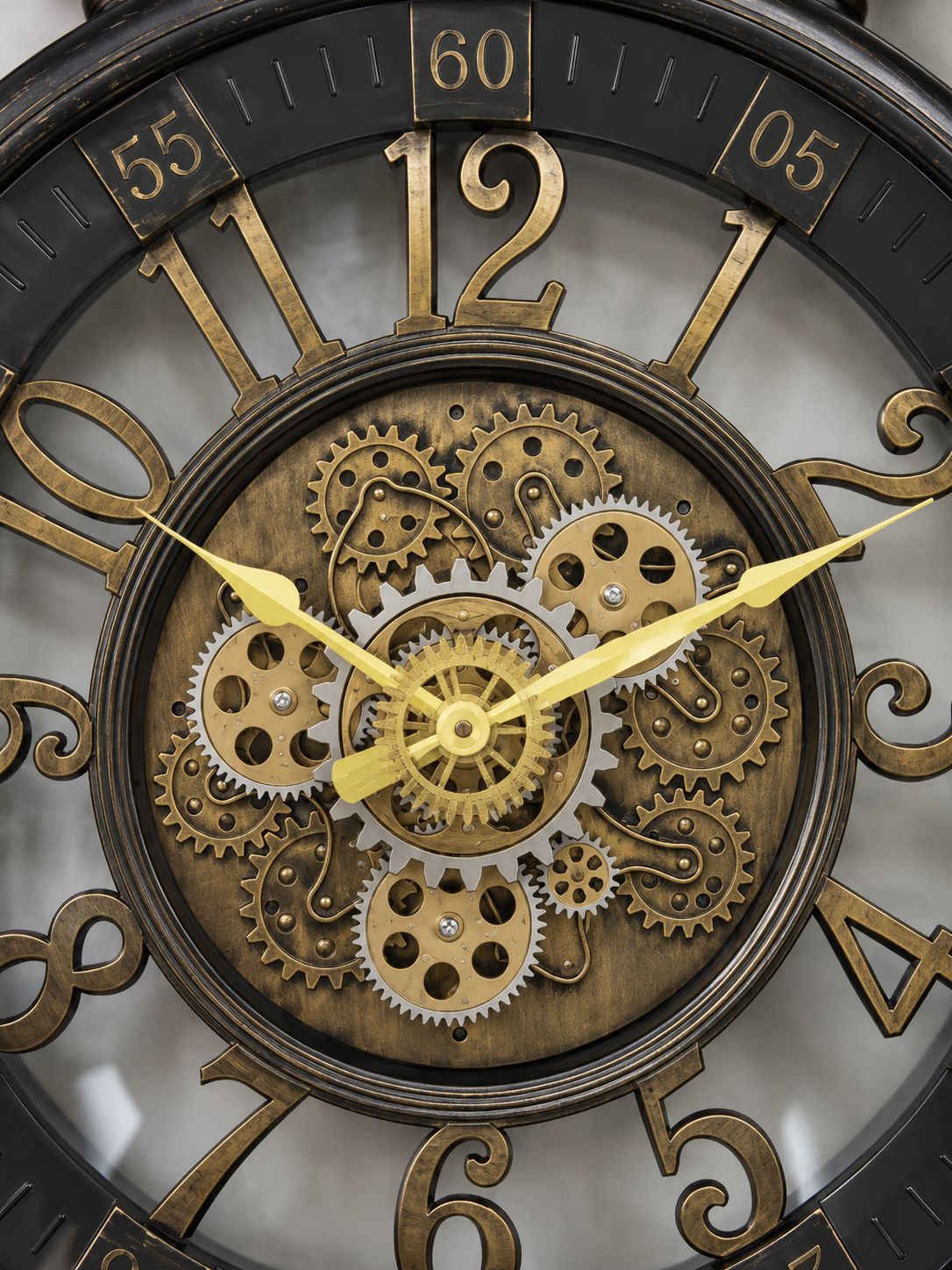 Close-up of a decorative wall clock face with large gold-tone numerals, a central exposed gear mechanism, and gold hands on a dark round frame.