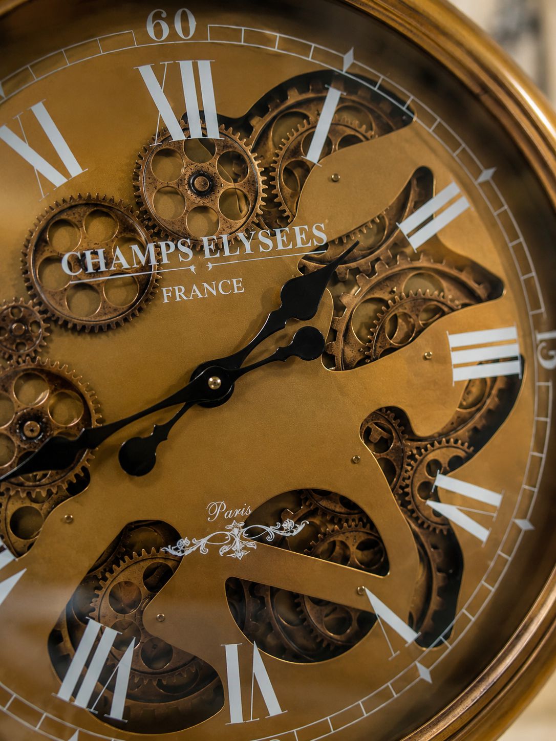 Close-up of a gold clock face with visible gears and 'Champs Elysees France' branding.