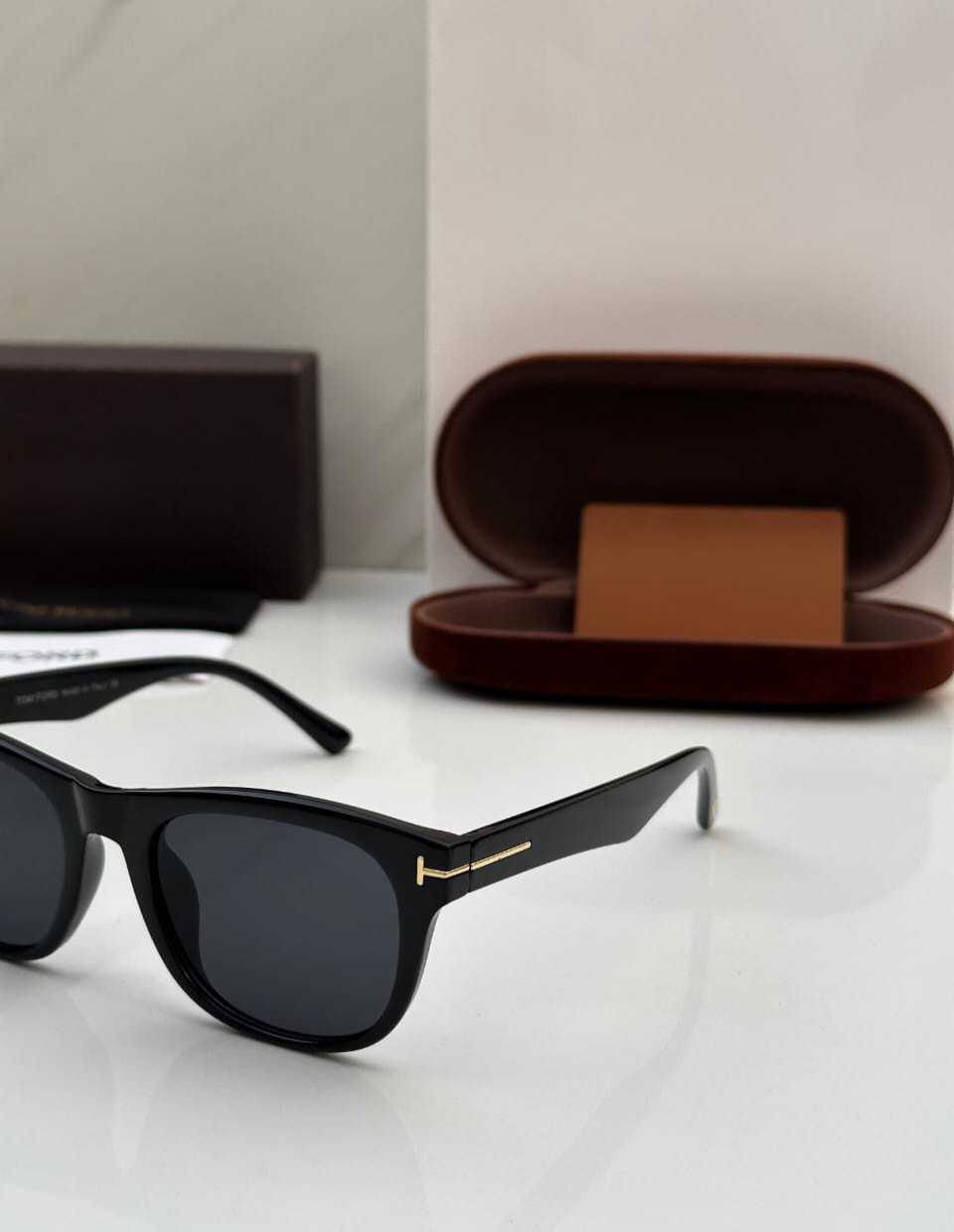 Close-up of black square sunglasses showing the gold 'T' detail and temple design.
