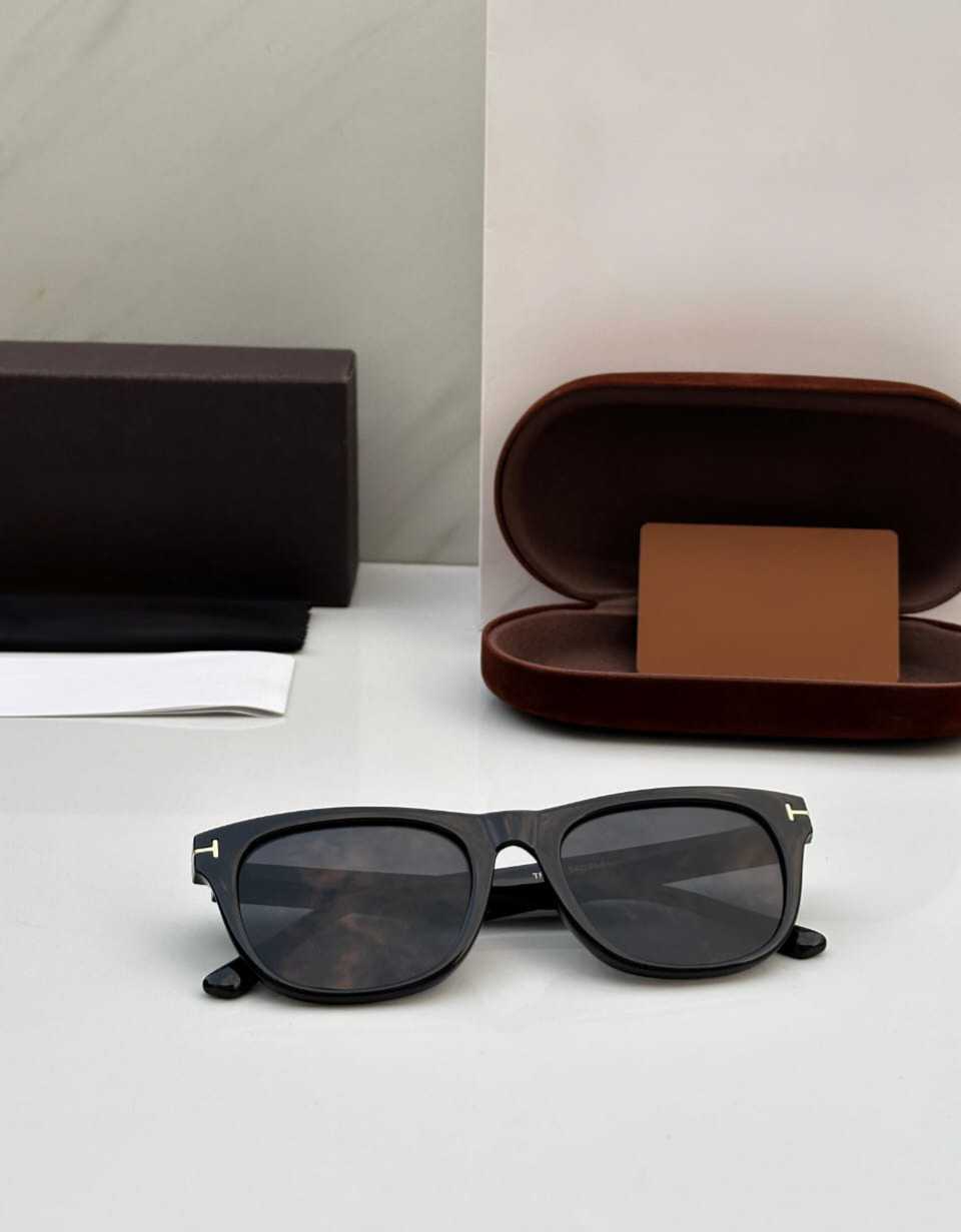 Close-up of black square sunglasses showing the gold 'T' detail and temple design.